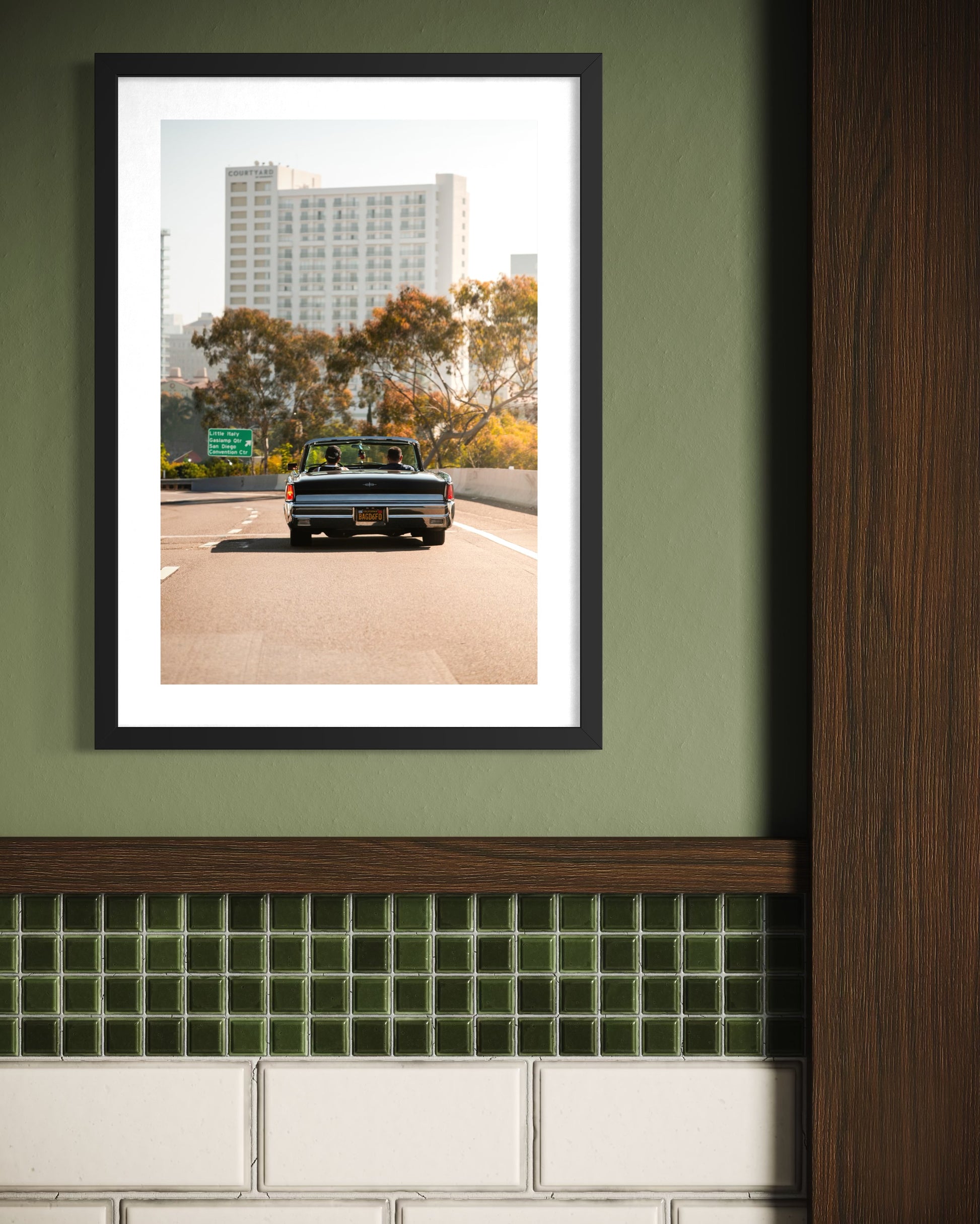 Framed photograph of a truck on a road with trees and buildings in the background, displayed on a green wall.